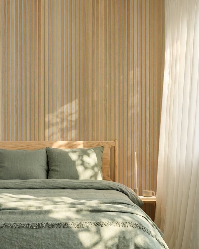 Minimalist Nordic bedroom featuring sage green bedding and a WoodUpp Classic Oak Akupanel acoustic slatwall; sunlight creates soft shadows on the bed.