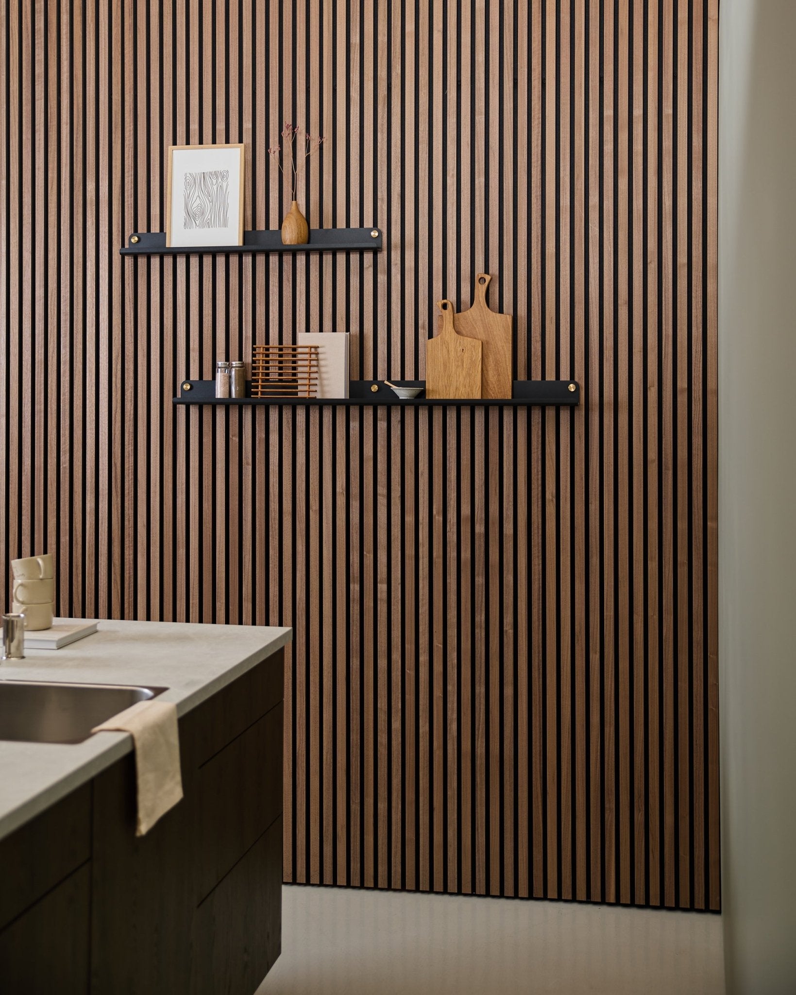 Modern kitchen featuring a Nordic-style acoustic slatwall panel, a black WoodUpp Norr Narrow Shelf (115.9 cm) for decor, and a towel draped over the sink.