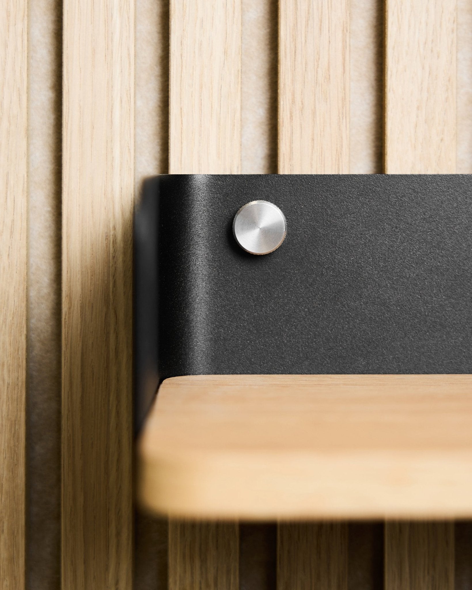 Close-up of a light wood shelf with black metal bracket, mounted using WoodUpp Finger screws (M5x10 mm, stainless steel), paired with Nordic acoustic panel.