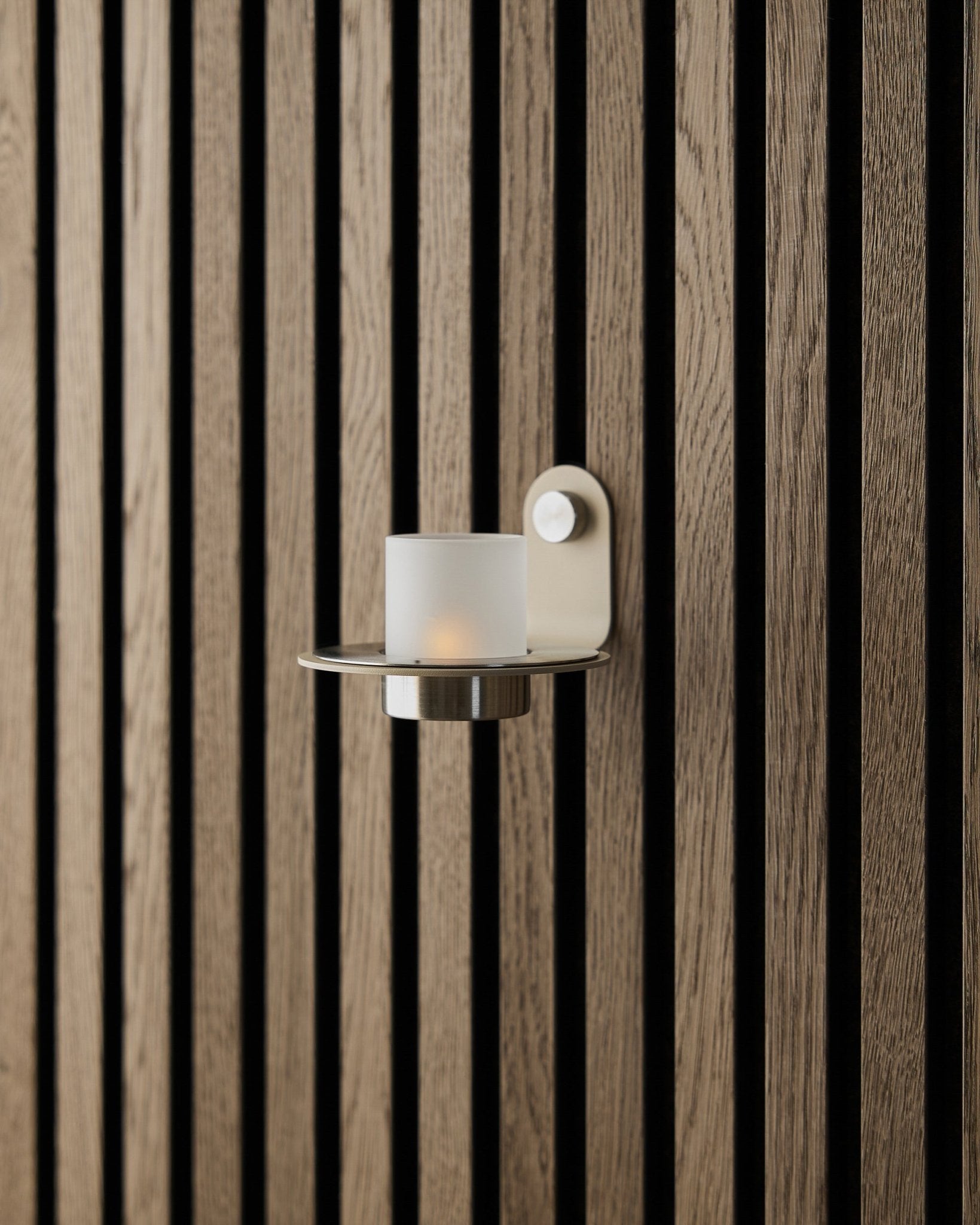 The Norr Candle Holder in beige stainless steel by WoodUpp displayed on a beige Akupanel acoustic panel wall.