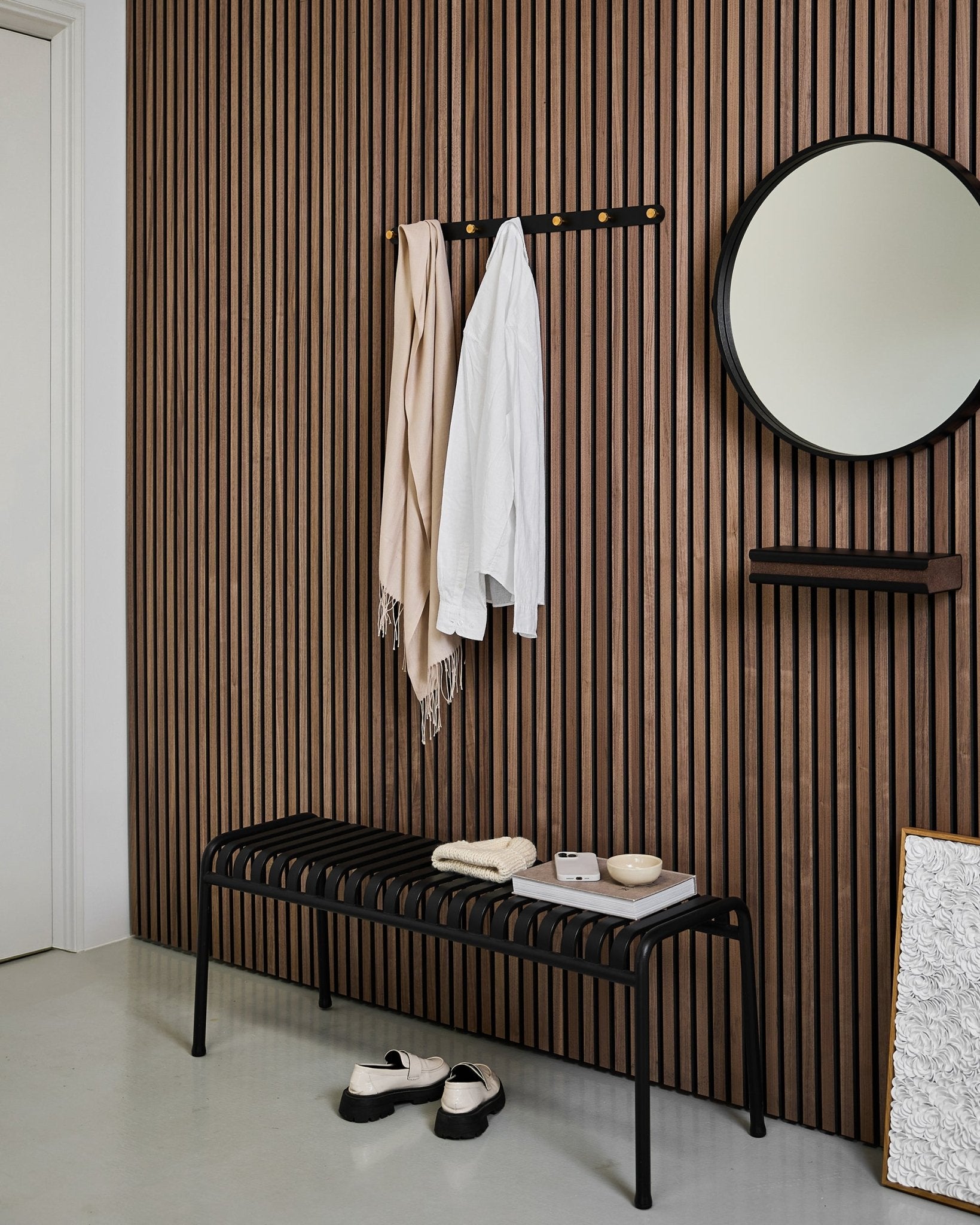 Minimalist entryway with a WoodUpp Akupanel acoustic slat wall, Norr Coat Hook Rack (Black/Brass, X7), bench, mirror, and modern neutral decor.