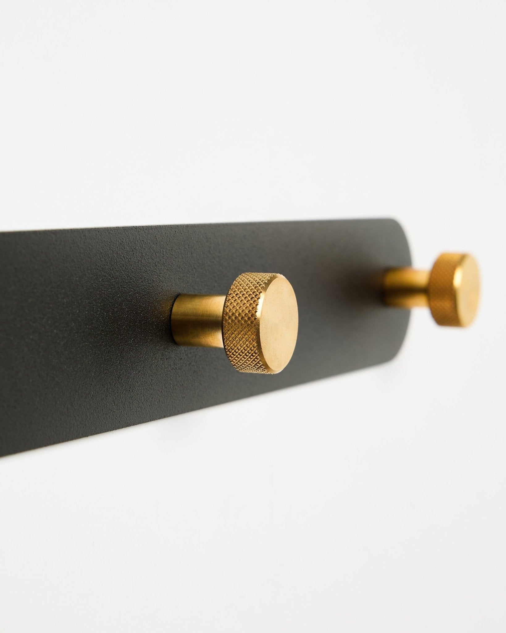 WoodUpp Norr Coat Hook Rack, model X7, featuring two cylindrical black and brass hooks on a black mount, displayed against a white background.