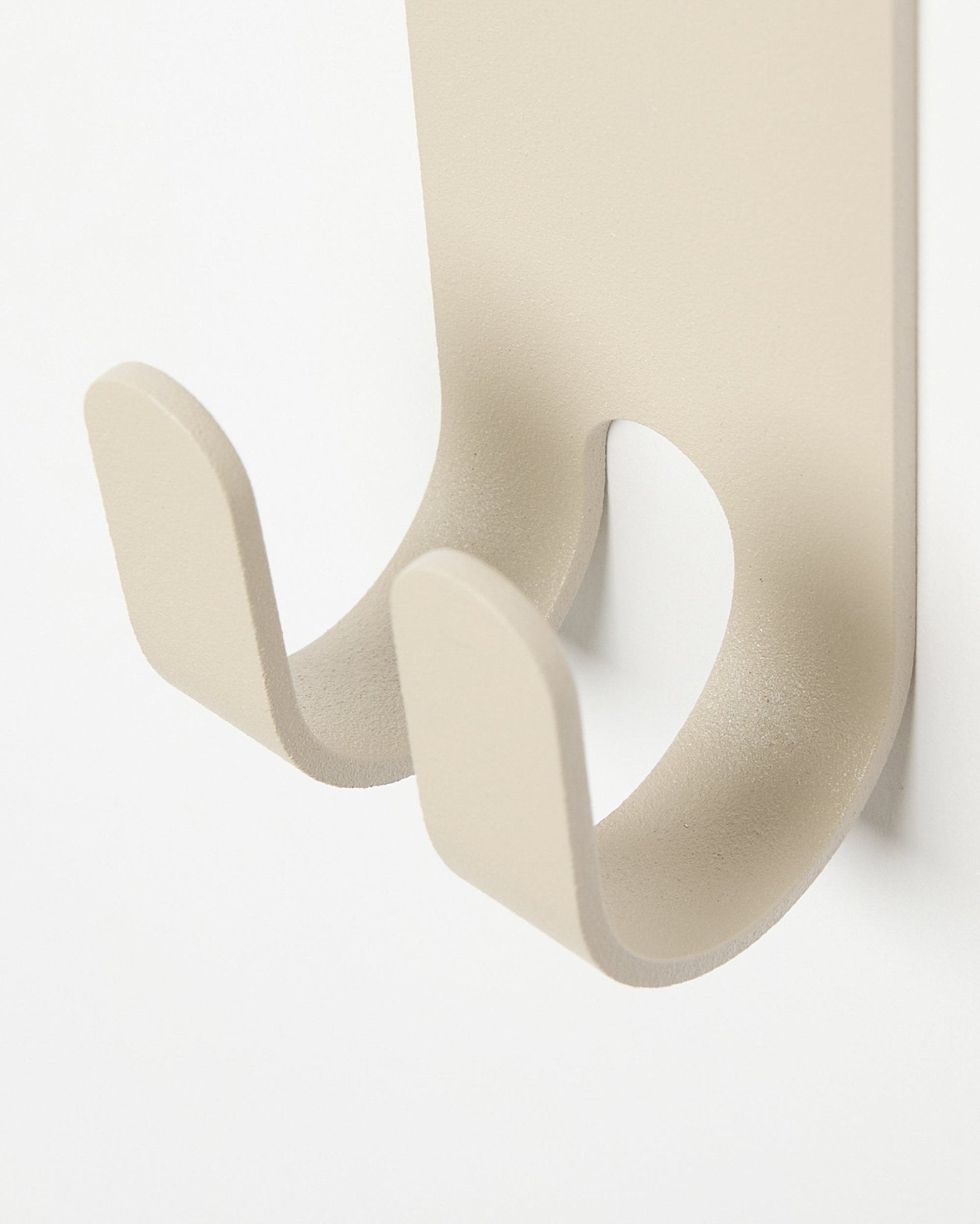 Close-up of the Norr Double Hanger in beige by WoodUpp, a minimalist metal coat hook installed on a light-colored acoustic panel.