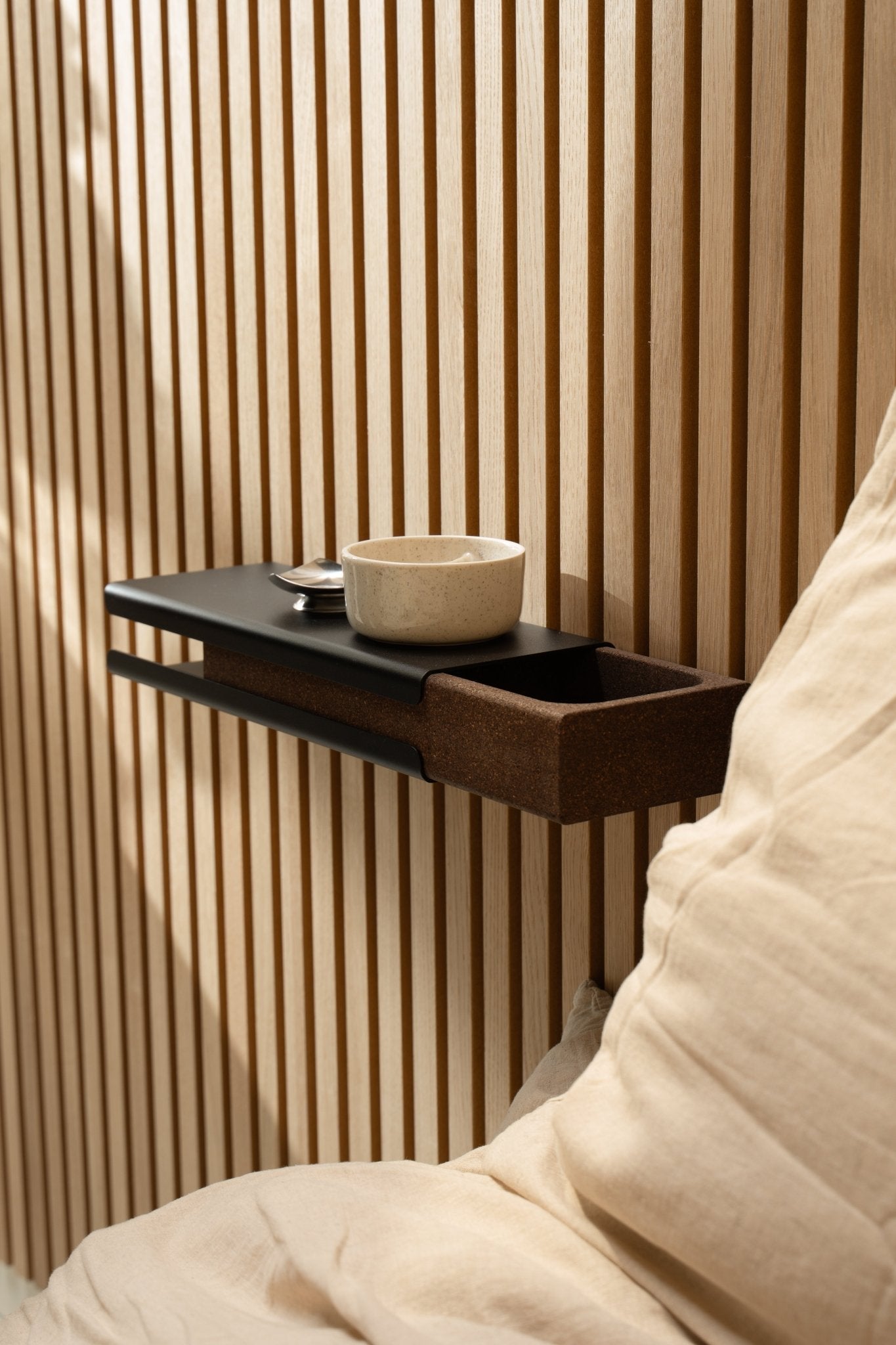 Minimalist wall shelf with a ceramic bowl and WoodUpp Norr Key Tray beside a beige cushion and Akupanel acoustic panel, illuminated by soft natural light.